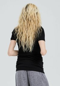 Black ribbed short-sleeve top paired with gray sweatpants. Long wavy blonde hair is visible. Smooth texture visible on fabrics.