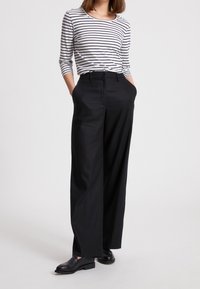 Pantaloni larghi neri realizzati in tessuto morbido, abbinati a un top a maniche lunghe bianco e blu a righe. Presentano una vita aderente e tasche.