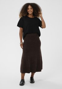 Črna majica s kratkimi rokavi združena z rjavo, srednje dolgo, teksturirano krilo. Črne copate zadržijo celoten videz.