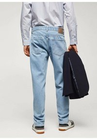 Jeans de mezclilla de color azul claro con un corte recto, bolsillos traseros y un parche de cuero marrón. Combinados con un blazzer azul marino y zapatos deportivos.