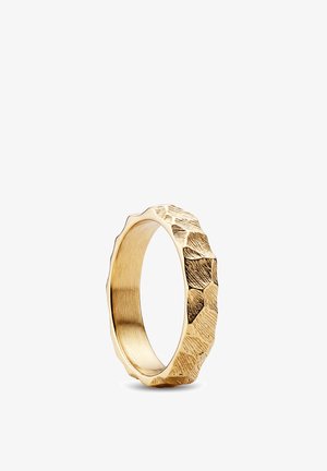 Goldener Ring mit strukturierter, facettierter Oberfläche und unregelmäßigem, gehämmertem Muster, der auf einem weißen Hintergrund aufrecht steht.