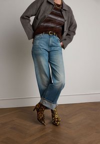 Jean haute taille bleu clair avec une coupe relax et des ourlets retroussés, associé à un pull rayé marron et des bottines à imprimé léopard.