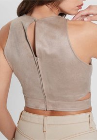 Kobieta w bezrękawnikowej, taupe crop topie z subtelny wzorem i suwakiem z tyłu, w towarzystwie jasnobeżowych spodni z wysokim stanem.