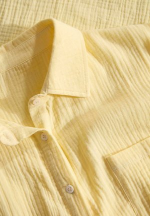 Lichtgele knoopshirt met een gestructureerde stof, voorzien van een puntkraag, twee knopen en een borstzak.