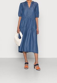 Denim midi-klänning med djup V-ringning, puffärmar och rynkade lager; matchad med en strukturerad krämfärgad väska och sandaler med blockklack i flera färger.