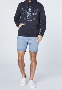 Mörkblå hoodie med central grafik och framficka, tillsammans med ljusblå uppvikta shorts och vita sneakers.