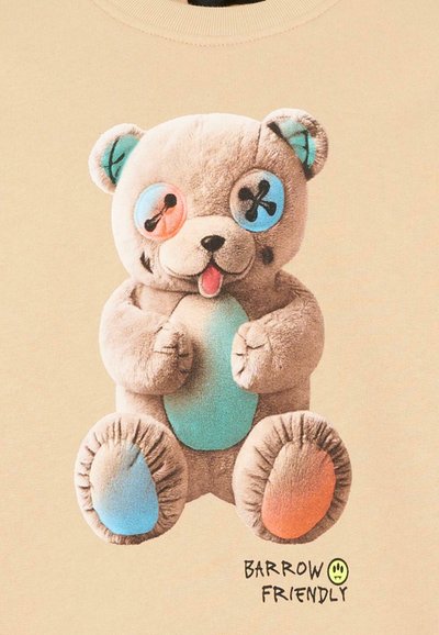 Ours en peluche avec des oreilles réparées dépareillées, des yeux en boutons multicolores, un ventre bleu, et une patte bleue et une patte orange, la langue tirée.