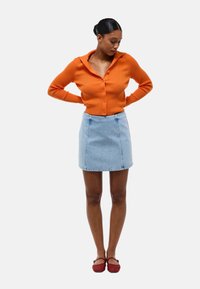Cardigan côtelé orange avec un col, associé à une mini-jupe en denim bleu clair et des chaussures tissées rouges. Vue à plat, sans motifs ni accents.