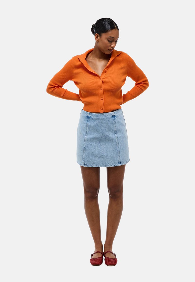 Cardigan côtelé orange avec un col, associé à une mini-jupe en denim bleu clair et des chaussures tissées rouges. Vue à plat, sans motifs ni accents.