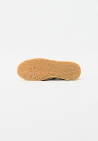 Talpă din cauciuc pentru tenisi cu un model de aderență, având un logo circular la călcâi și o nuanță de bej contrastantă. Textură netedă în ansamblu.