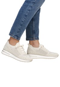 Weiße Strick-Sneakers mit einem strukturierten Muster, Schnürverschluss und einer gepolsterten Sohle, kombiniert mit hochgekrempelten blauen Jeans.