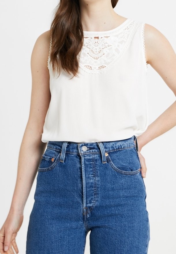 Biała bluzka bez rękawów z koronkowym wykończeniem przy dekolcie. Połączona z wysokim stanem niebieskich dżinsów. Gładki materiał, luźny krój.