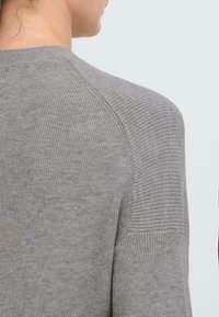 Grauer gestrickter Pullover mit Rippstruktur, Raglanärmeln und rundem Halsausschnitt. Der Stoff sieht weich und leicht aus.