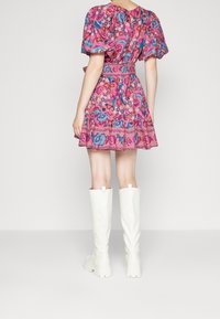 Vestido corto rosa con estampado floral, mangas abullonadas y cintura ceñida con cinturón, combinado con botas gruesas blancas hasta la rodilla.