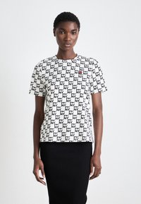 T-maica kratkih rukava u bijeloj boji s crnim NY uzorkom. Ima okrugli izrez i mali crveni logotip na lijevoj strani prsnog koša.