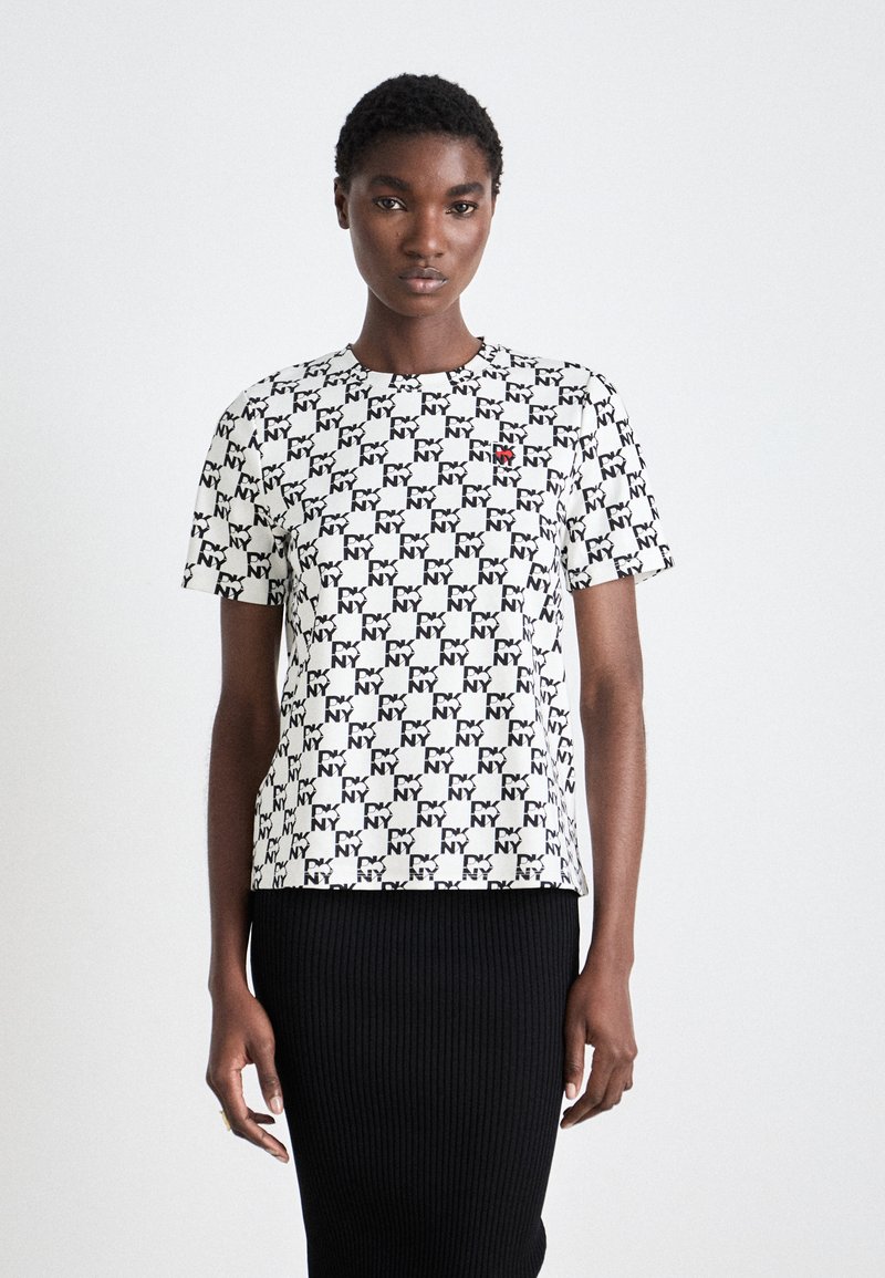 T-maica kratkih rukava u bijeloj boji s crnim NY uzorkom. Ima okrugli izrez i mali crveni logotip na lijevoj strani prsnog koša.