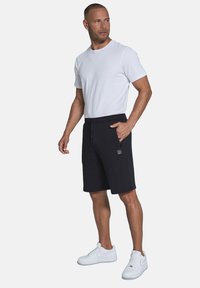 Schwarze Shorts mit einem elastischen Bund und Kordelzug, kombiniert mit einem enganliegendem weißen T-Shirt und weißen Sneakers. Flachnahtdetails sind sichtbar.