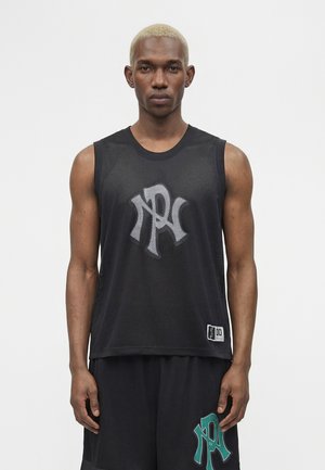 Jeune homme aux cheveux blonds courts portant un haut en maille noire sans manches et un short assorti, tous deux ornés d’un logo stylisé vert et blanc à l’avant.