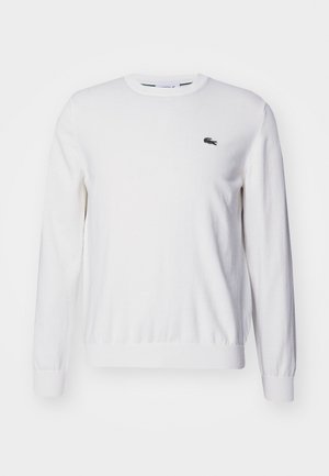 Hvid langærmet sweater med rund halsudskæring, ribbede manchetter og kant, med et lille broderet logo i sort og grøn på brystet.