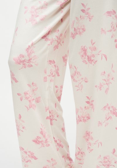 Gros plan sur un pantalon en tissu couleur crème avec un motif floral rose doux et une coupe ample et décontractée.