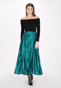 Vállnélküli fekete felső, amelyet egy redőzött teal szatén szoknyával párosítanak. A szoknya elasztikus derékpánttal rendelkezik, és a vádli közepéig ér.