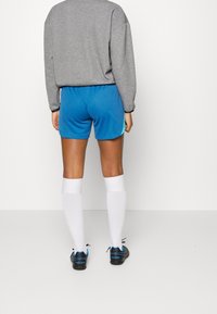 Top de manga larga gris combinado con pantalones cortos deportivos azules con un patrón texturizado, calcetines blancos hasta la rodilla y zapatos deportivos negros.