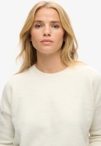 Sweter w kolorze kremowym, lekki, o okrągłym dekolcie i długich rękawach, charakteryzujący się miękką teksturą i minimalistycznym designem.