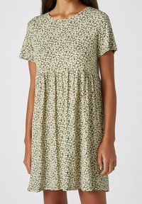 Robe à manches courtes en tissu vert à motif floral blanc, avec un col rond et une taille froncée pour une coupe décontractée.