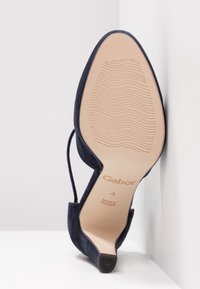 Chaussure à talon haut en daim bleu marine inclinée vers le haut, montrant la semelle beige à motif ondulé, taille 4, avec le texte « Gabor Made in Portugal ».