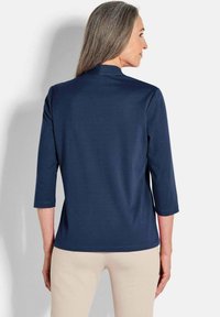 Marineblaue Bluse mit Dreiviertelärmeln aus weichem Stoff, die ein minimalistisches Design und einen leicht abgerundeten Saum aufweist.
