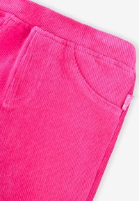 Pluizige roze corduroy stof met ribbeltextuur. Voorzien van een zijzak en een klein label. Nadruk op zachtheid en levendige kleur.
