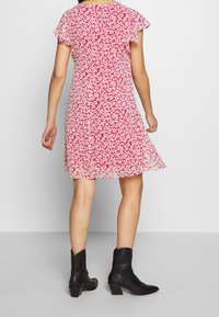 Röd blommig klänning med korta fladdrande ärmar, A-linjeform och semi-genomskinligt tyg. Bärs med svarta ankelstövlar.