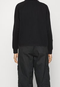 Fitted svart sweatshirt med raglanärmar, ribbade muddar och nederkant. Matchas med löst sittande svarta cargobyxor med sidofickor.