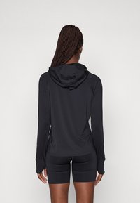 Pikad varrukadega must spordimütsiga ülemine osa, millel on pehme tekstuur, reguleeritav kapuuts ja pöidlate augud; kombineeritud mustade lühikestega.