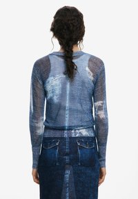 Blue knit sweater with denim print, long sleeves, ribbed hem, and a fitted design. Worn over a matching denim-patterned skirt.