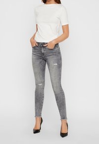 Jeans skinny grises con detalles desgastados, combinados con una camiseta blanca ajustada de manga corta y zapatos de tacón alto negros.