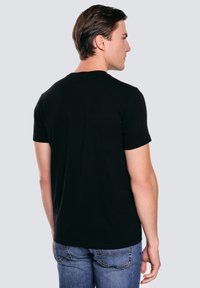 Černé bavlněné tričko s krátkými rukávy, kulatým výstřihem a hladkým povrchem, doplněné o vybledlé modré džíny. Zobrazeno ze zadní strany.