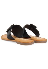 Sandales nu-pieds en cuir noir avec une large bride et un nœud décoratif. Présente une semelle intérieure rembourrée beige et une semelle extérieure en caoutchouc marron.