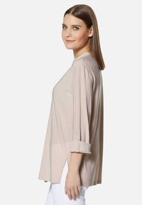 Hellbeige Langarmshirt aus glattem Stoff, mit einer lockeren Passform, hochgerollten Ärmeln und seitlichen Schlitzen für zusätzlichen Komfort.