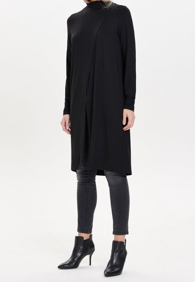 Femme portant une longue tunique noire à manches longues, un jean skinny gris foncé et des bottines noires à bout pointu avec talons.