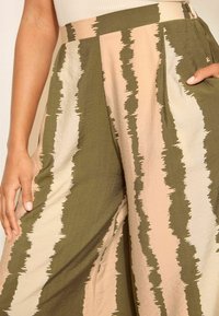 Kalhoty s širokými nohavicemi z lehkého materiálu s zeleno-bežovým zigzag vzorem. Obsahují boční kapsy a vysoký pas.