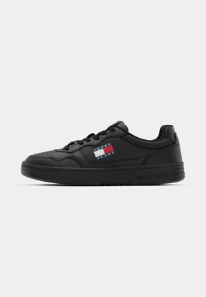 Schwarze Sneakers aus glattem Synthetikmaterial, mit einer niedrigen Oberkante, Schnürverschluss und einem LOGO-Patch mit rot, weiß und blau Akzenten.