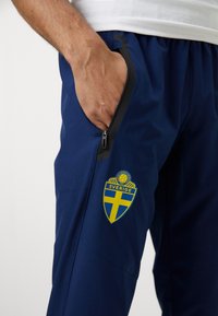 Ναυτικές αθλητικές παντελόνες με πλαϊνές κρυφές τσέπες και αναπνεύσιμο υλικό. Διαθέτουν μπλε και κίτρινο έμβλημα της Σουηδίας στο μηρό.