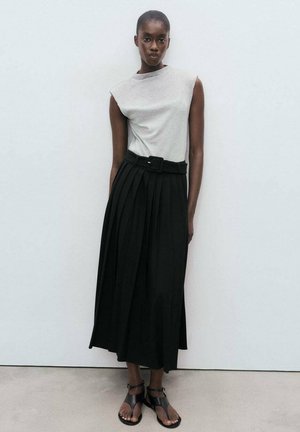 Top gris sin mangas, falda negra plisada con cinturón y sandalias negras con tiras. Tejido suave, forma estructurada, diseño hasta el tobillo.