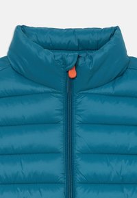 Teal pufferjack met verticale quilted structuur, hoge kraag en rits aan de voorkant met een oranje trekband. Licht en geïsoleerd ontwerp.