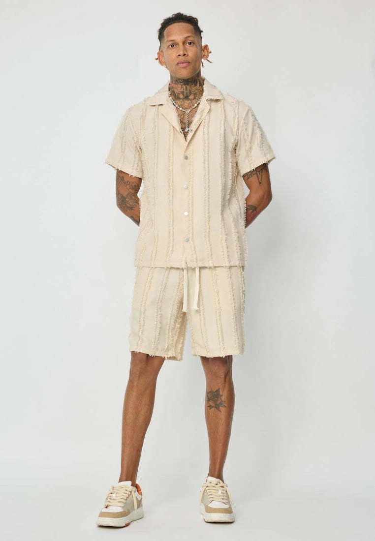 Chemise beige à manches courtes avec des rayures en relief, associée à un short assorti. Coupe décontractée avec cordon de serrage et tissu texturé.