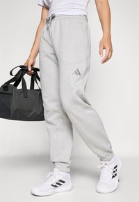 Sive trenirke, izdelane iz mehkega blaga, z elastičnim pasom in manšetami. V kombinaciji z belimi športnimi copati z črnimi detajli. Črna športna torba.