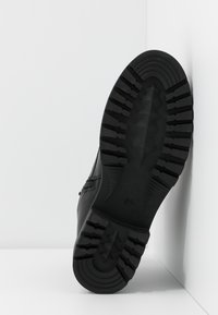 Baskets noires avec semelle en caoutchouc texturée, présentant un motif de bande de roulement géométrique. Tige en matériau lisse et durable avec des ornementations minimales.