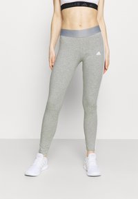 Leggings grigi con una vita alta e strisce laterali bianche, realizzati in un materiale morbido e elasticizzato. Presentano il logo Adidas sulla coscia.