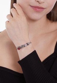 Silver charm bracelet with red and silver beads, featuring a mix of circular and square shapes, displayed on a wrist.